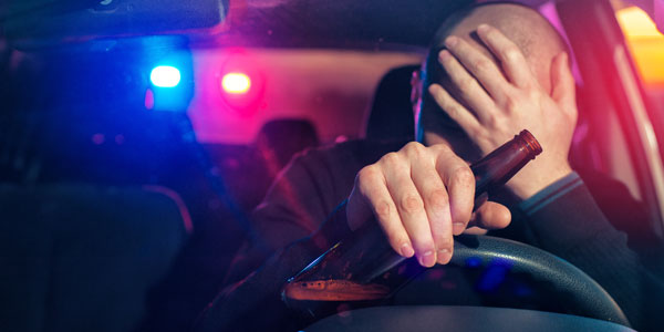 Drinking while at the wheel of a car. One hand on the bottle the other on the head