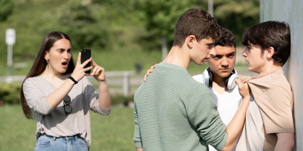 A young person being threatened by two others while another films the scene using their moble phone