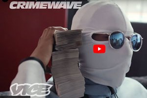 A figure in a mask holding a pile of note shaped paper on his shoulder